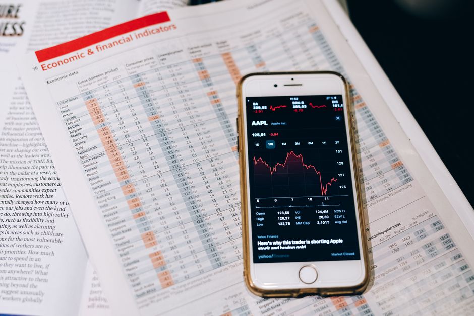 Imagem de uma tela de smartphone exibindo gráficos de ações sobre um relatório financeiro, simbolizando análise de mercado e investimentos.
