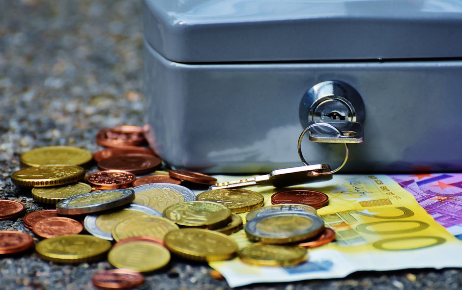 Imagem de um cofre ao lado de moedas e cédulas, simbolizando segurança financeira e economia.