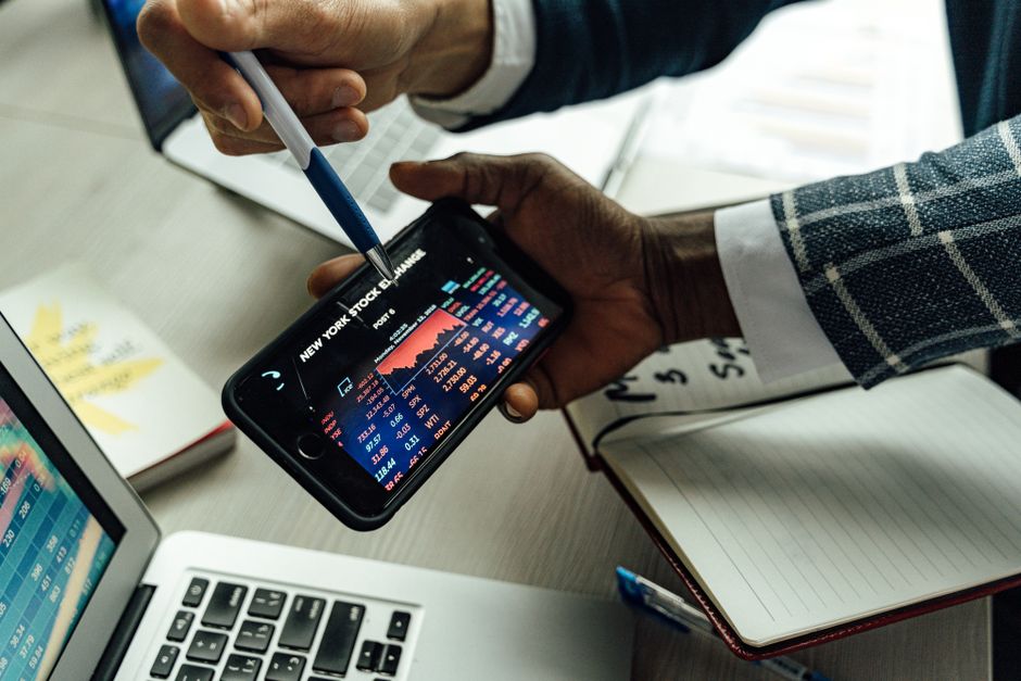 Pessoas analisando gráficos de mercado financeiro em um ambiente de negócios, com uso de tecnologia para tomada de decisões de investimentos.