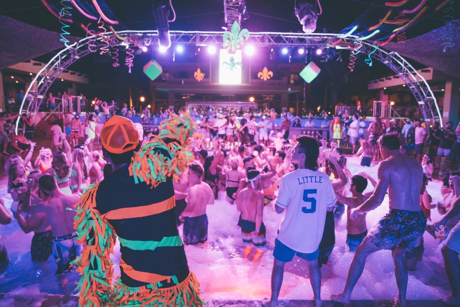 Pessoas se divertindo em uma piscina com iluminação colorida durante uma festa temática noturna.