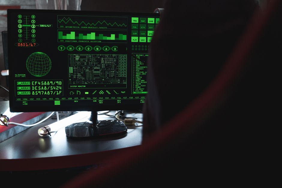 Imagem de uma pessoa observando uma tela de monitor com gráficos e códigos relacionados à tecnologia e segurança digital.