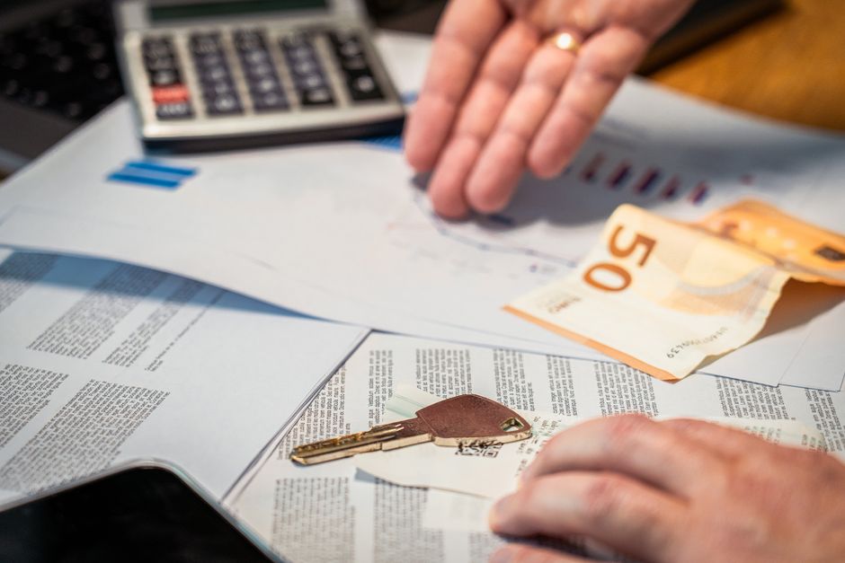 Pessoa controlando suas finanças pessoais com planilhas, dinheiro em papel e uma calculadora em um ambiente de escritório ou estudo.