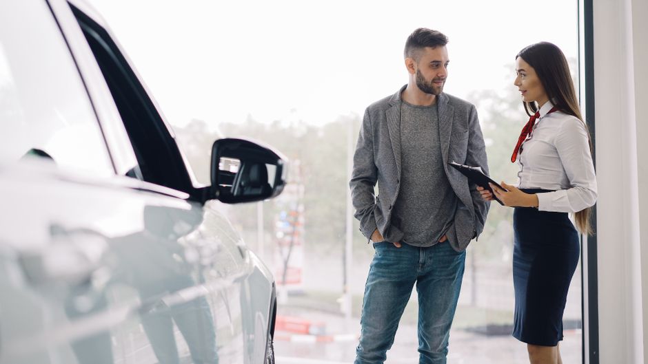 Homem atendendo uma mulher na concessionária de veículos, representando negociação ou venda de carros.