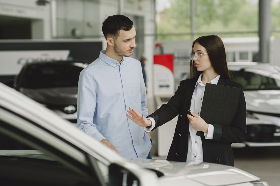 Imagem de uma mulher atendendo um cliente em uma concessionária de carros, exemplificando atendimento ao cliente e vendas automotivas.