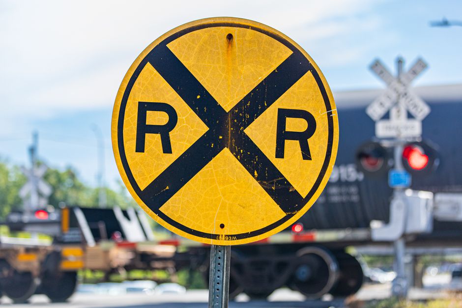 Placa de aviso de trem crossing com um trem ao fundo, destacando a importância da segurança em áreas de passagem de trens.