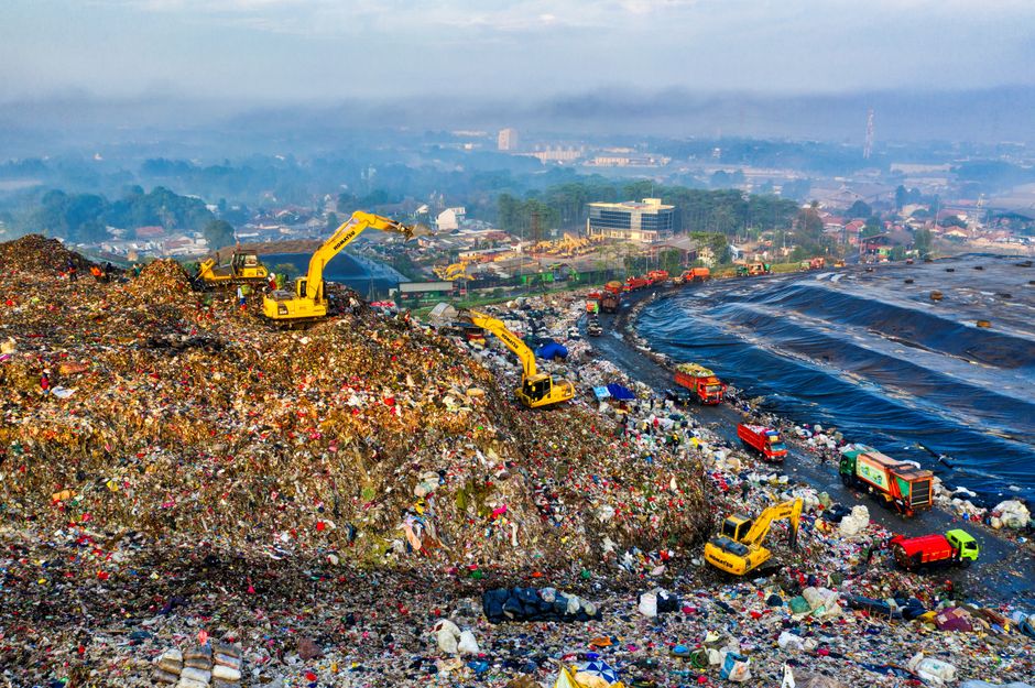 Paisagem de um lixão a céu aberto com escavadeiras operando entre lixo acumulado, destacando os problemas ambientais do descarte de resíduos.