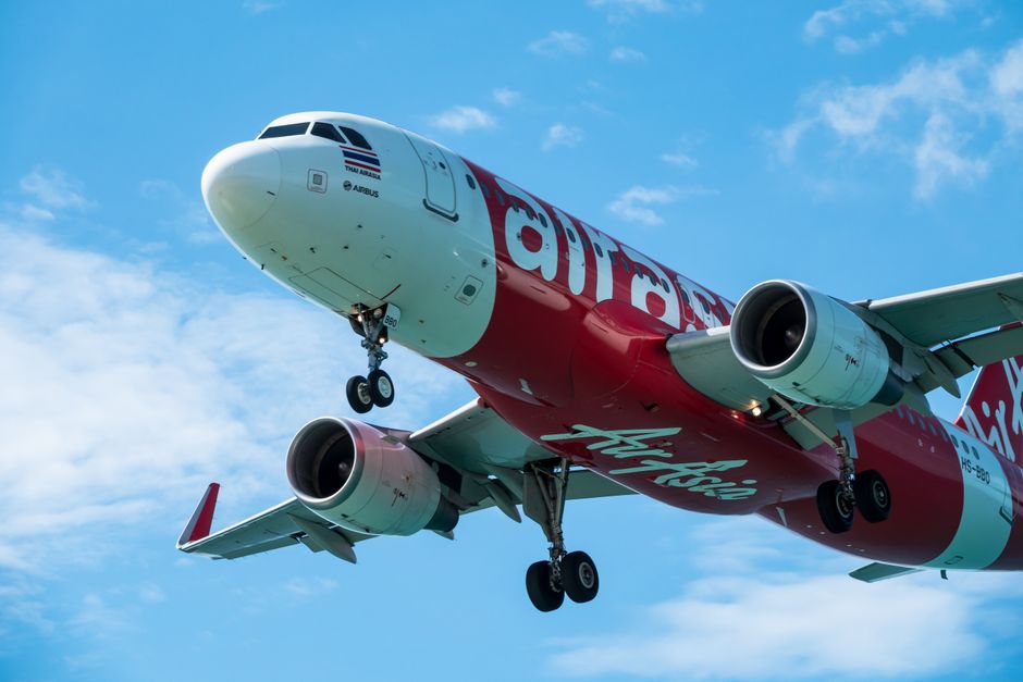 Avião da companhia aérea AirAsia em voo de aproximação com céu claro ao fundo, representando transporte aéreo econômico.