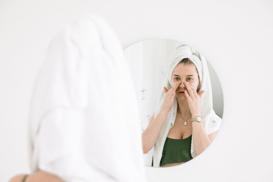 Mulher cuidando da pele ao aplicar um produto facial diante de um espelho, em um momento de cuidado pessoal e rotina de beleza.