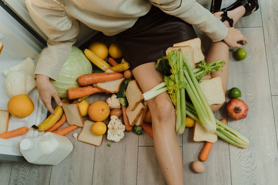 Pessoa deitada no chão cercada de alimentos e pão, transmitindo uma sensação de sobrecarga ou descontrole na alimentação.