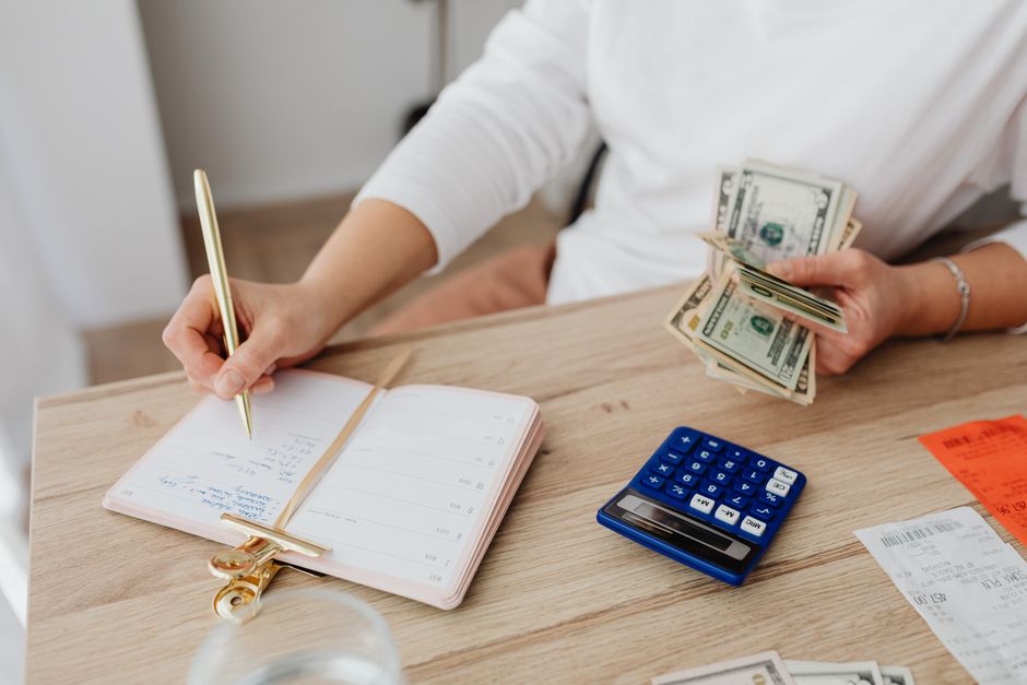 Pessoa fazendo planejamento financeiro com dinheiro, caderno, calculadora e recibos sobre uma mesa de trabalho
