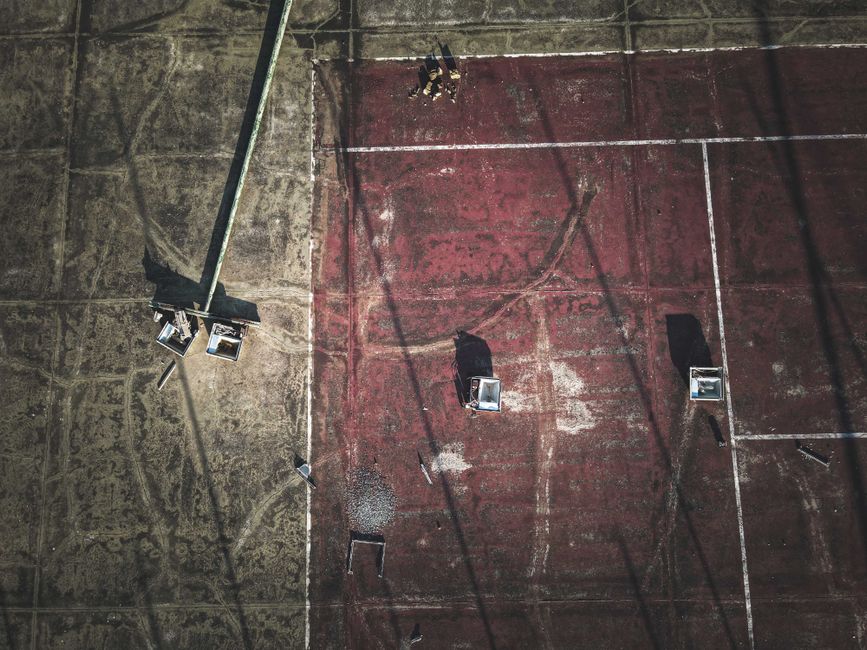 Imagem de uma quadra de basquete ao entardecer, com sombras alongadas e iluminação artificial, transmitindo uma atmosfera de esportes e lazer ao ar livre.