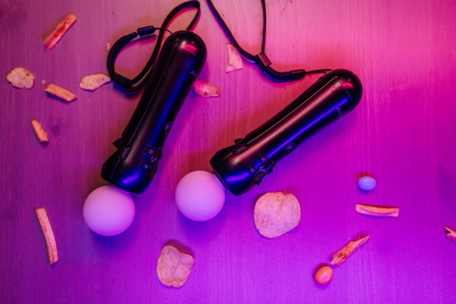 Imagem de dois dispositivos de luz portáteis em um ambiente com iluminação colorida, acompanhados por snacks espalhados na superfície de um balcão ou mesa.