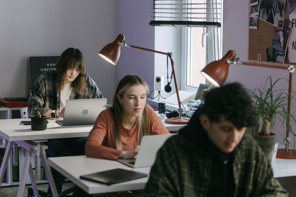 Jovens estudantes concentrados em sala de aula com laptops, demonstrando foco e aprendizado em ambiente acadêmico.