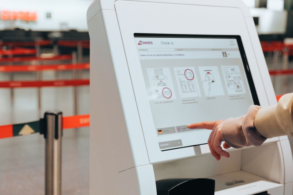 Pessoa utilizando um quiosque de auto check-in no aeroporto, simbolizando praticidade e tecnologia na experiência de viagem.
