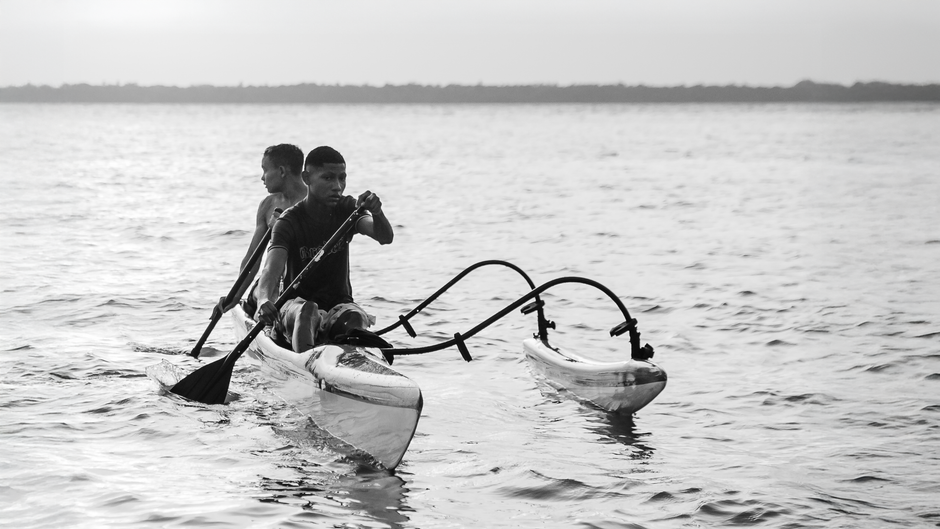 Dois jovens navegando em uma canoa com remos em um corpo de água, transmitindo uma sensação de aventura ou lazer ao ar livre.