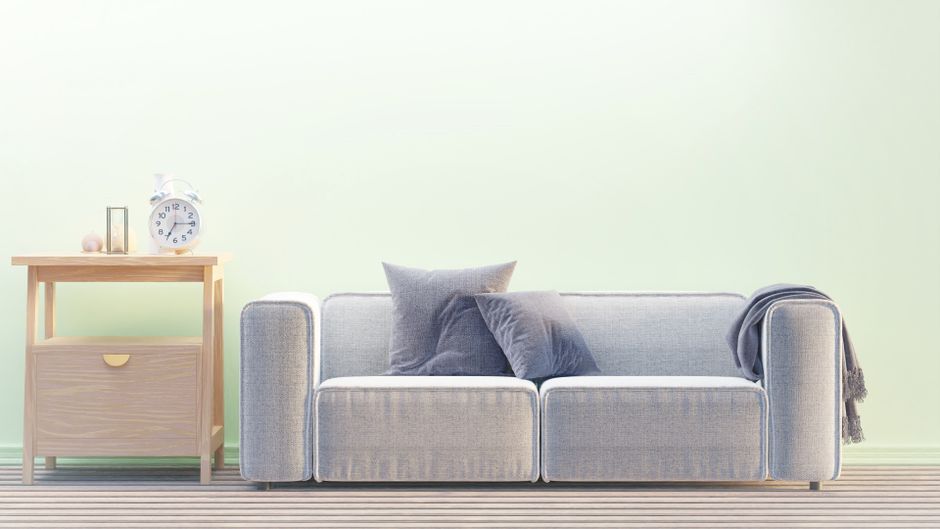 Imagem de uma sala de estar minimalista com sofá confortável, almofadas e uma mesa de cabeceira com relógio de mesa, ideal para artigos sobre decoração de ambientes e organização doméstica.