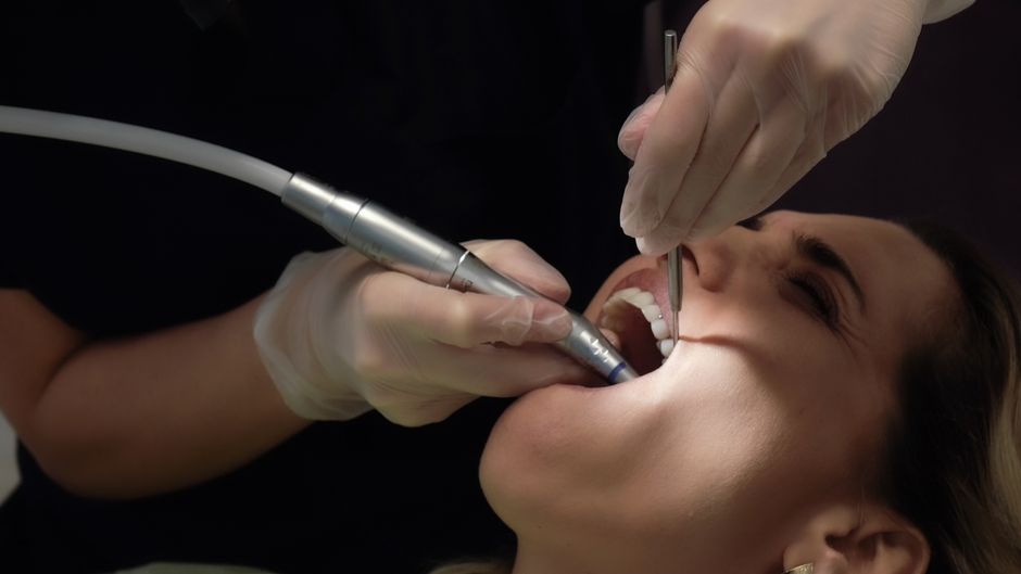 Procedimento odontológico estético, apresentando um dentista realizando um tratamento na boca de uma paciente em ambiente clínico.