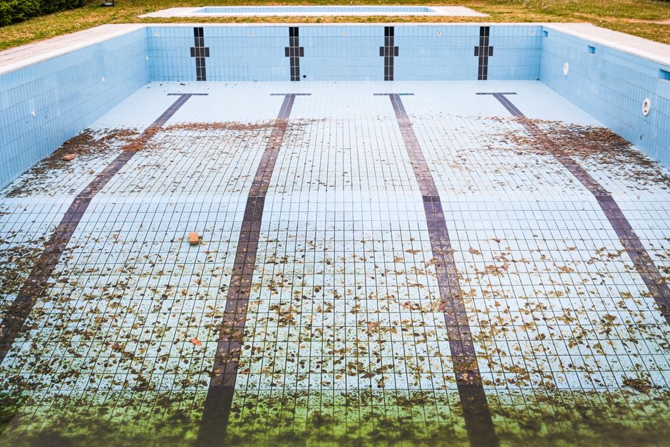 Piscina abandonada com águas sujas e folhas, simbolizando negligência no cuidado com espaços de lazer ao ar livre.