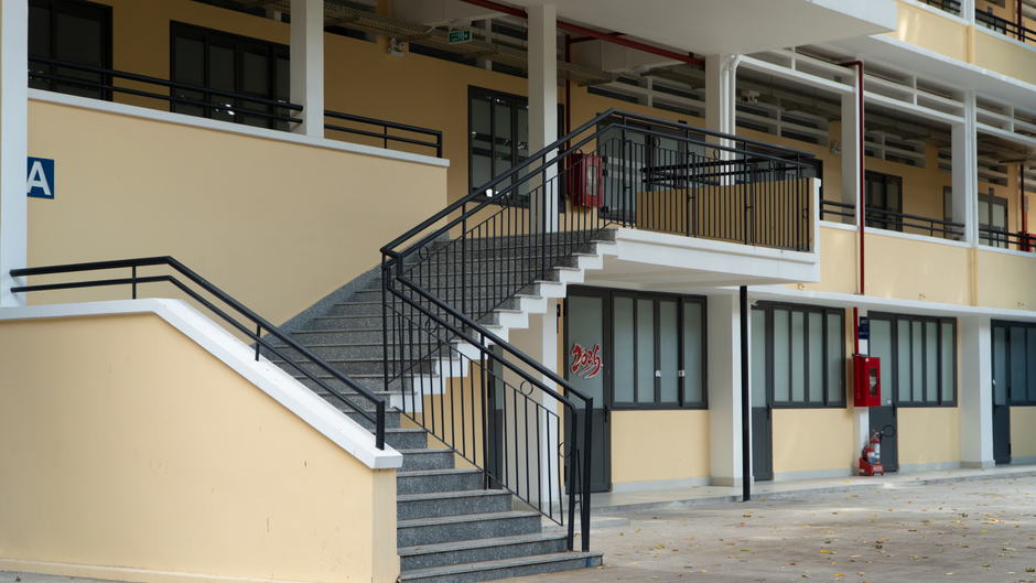 Imagem de um edifício comercial com escadaria externa, janelas grandes e elementos de segurança, representando infraestrutura urbana.