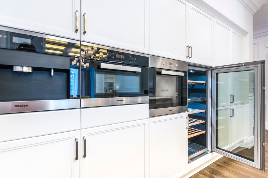 Imagem de uma cozinha moderna com forno embutido e uma geladeira de portas de vidro, destacando o design clean e elegante do espaço.
