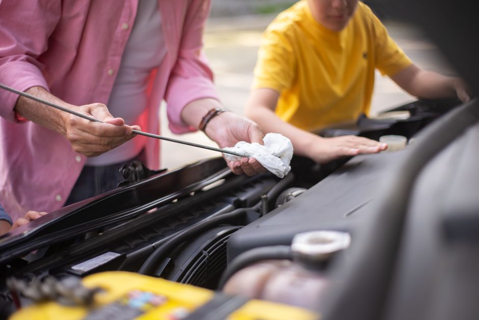 Homem e criança realizando manutenção em um carro ao ar livre, simbolizando ensino e aprendizado prático sobre mecânica automotiva.