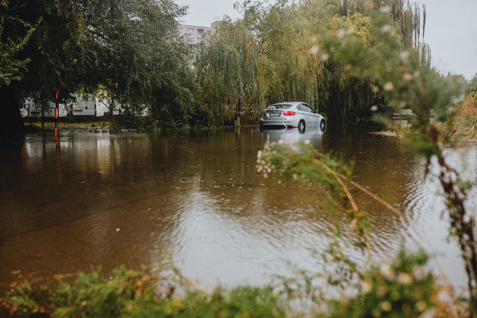 Carro parcialmente submerso devido a alagamento urbano causado por fortes chuvas.