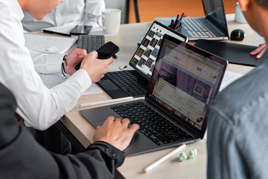 Reunião de equipe de trabalho colaborando em projetos de tecnologia e inovação com laptops, tablets e smartphones em uma sala de escritório.