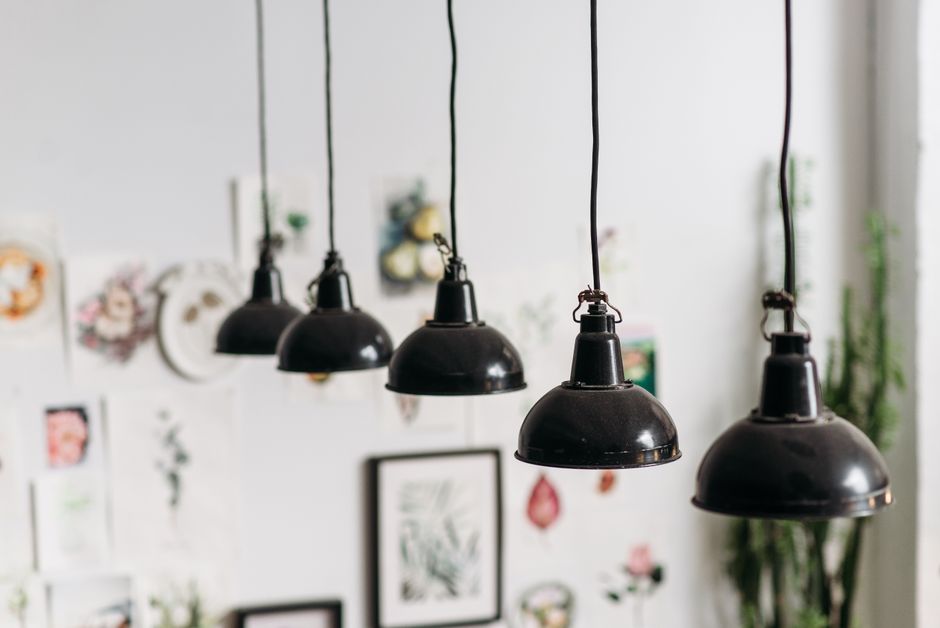 Iluminação moderna com luminárias pendentes em um ambiente de escritório decorado com quadros e plantas ao fundo.