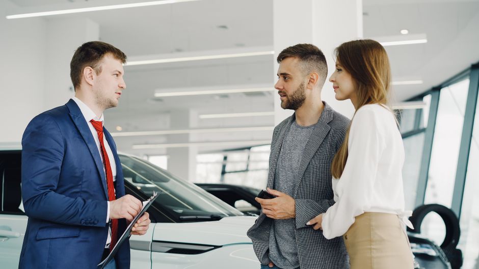 Homem conversando com um vendedor de carro sobre opções de compra em uma concessionária moderna.