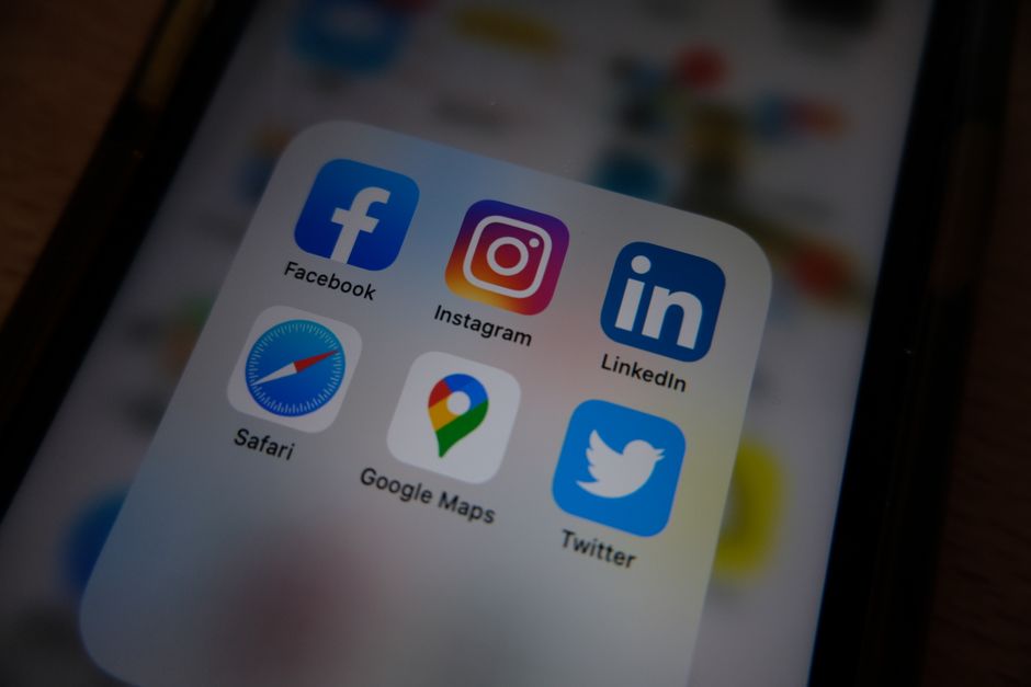 Imagem de um smartphone exibindo ícones de redes sociais como Facebook, Instagram, LinkedIn e Twitter, sugerindo o uso de plataformas digitais para comunicação e marketing.