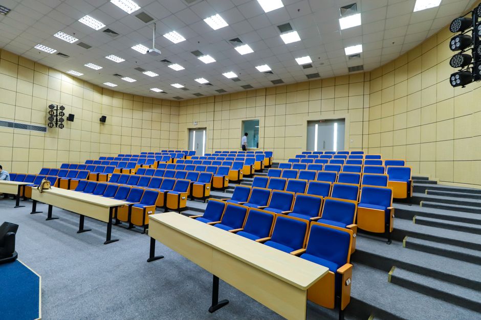 Auditório amplo com assentos em azul e iluminação de teto, ideal para eventos, palestras ou conferências.