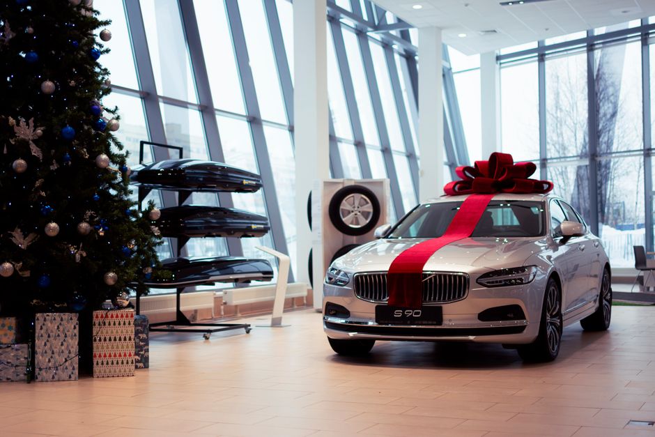 Carro de luxo decorado com um laço vermelho, em um ambiente de concessionária ou showroom, pronto para presente de fim de ano.