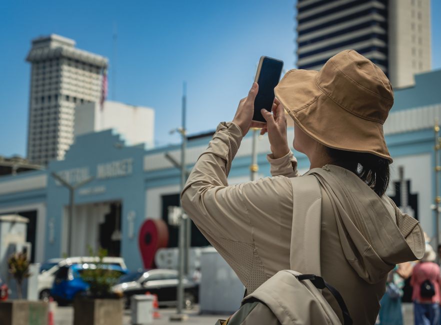 Pessoa tirando foto com smartphone em ambiente urbano, destacando o cenário de cidade moderna ao fundo.