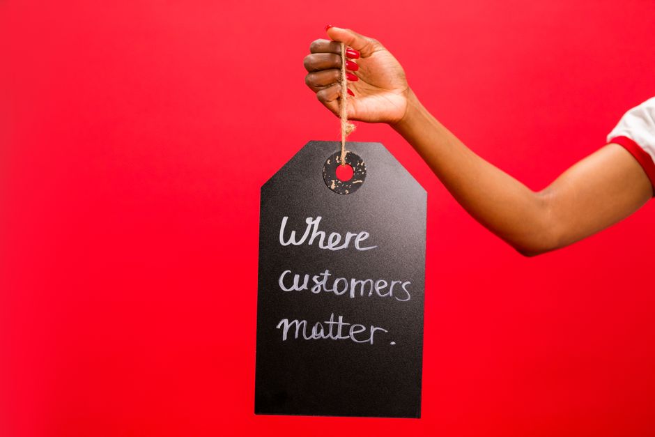 Pessoa segurando uma etiqueta com a frase 'Where customers matter' contra fundo vermelho, destacando a importância do relacionamento com o cliente em negócios.
