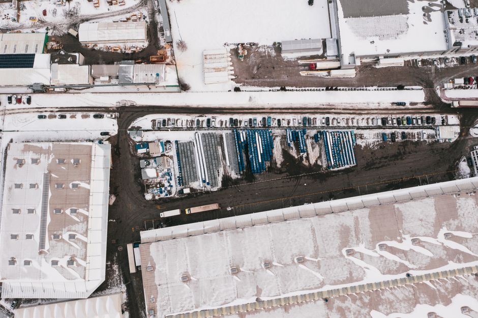Imagem aérea de um estacionamento de caminhões em uma área industrial com neve, destacando a logística e o transporte de cargas.