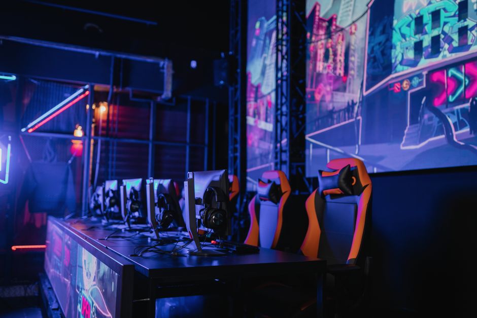 Estação de jogos de eSports com várias cadeiras, periféricos e uma tela grande com iluminação neon, destacando o ambiente de competição digital.
