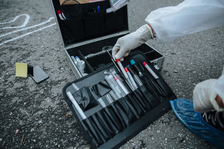 Imagem de uma pessoa usando luvas ao manusear equipamentos de coleta de amostras em uma ação de campo de laboratório ou investigação forense.