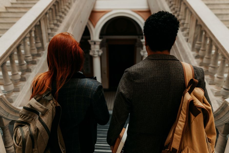 Imagem de dois estudantes ou jovens profissionais caminhando pelas escadarias de um prédio histórico ou universitário, simbolizando educação ou futuro profissional.