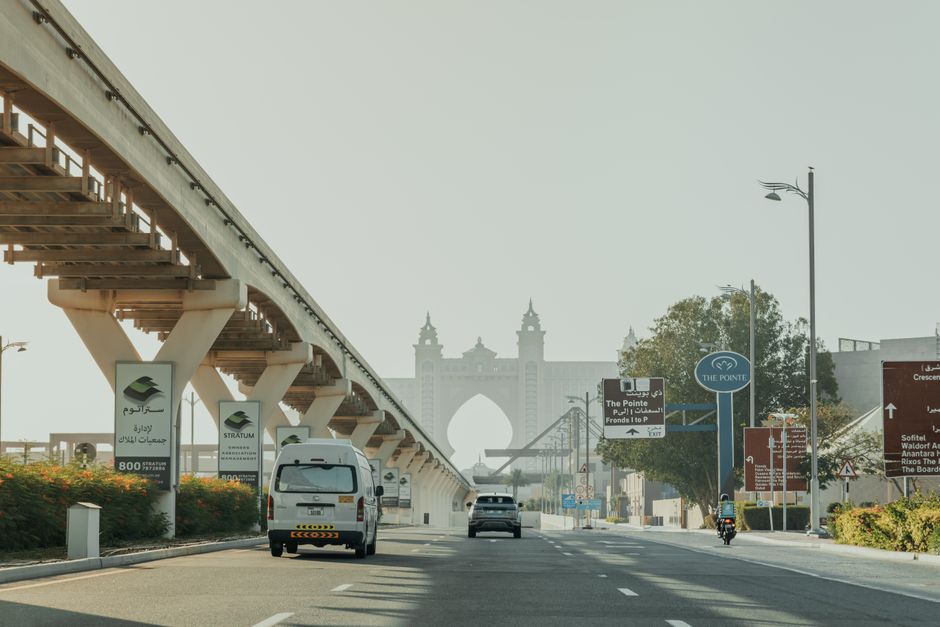 Imagem de uma rua urbana com um elevado e sinais de trânsito, incluindo uma estrutura arquitetônica ao fundo, transmitindo o tema de urbanismo e infraestrutura da cidade.