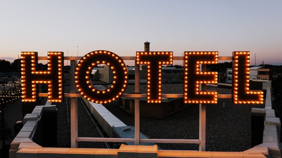 Placa de letreiros iluminados em uma construção de hotel ao entardecer, destacando a sinais de hospedagem e turismo.