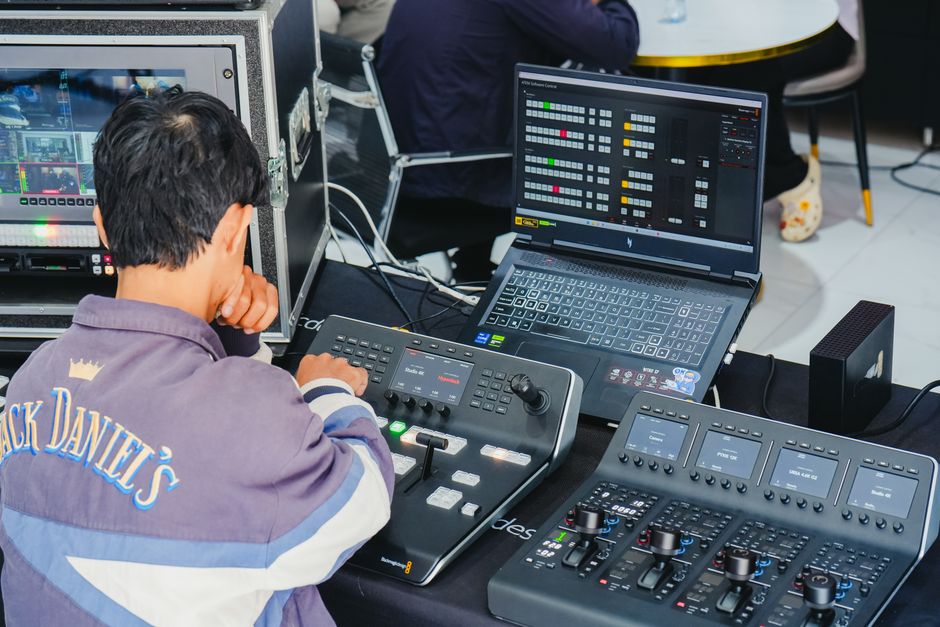 Imagem de uma pessoa operando equipamentos de áudio e monitoramento em um ambiente de produção musical ou transmissão ao vivo.