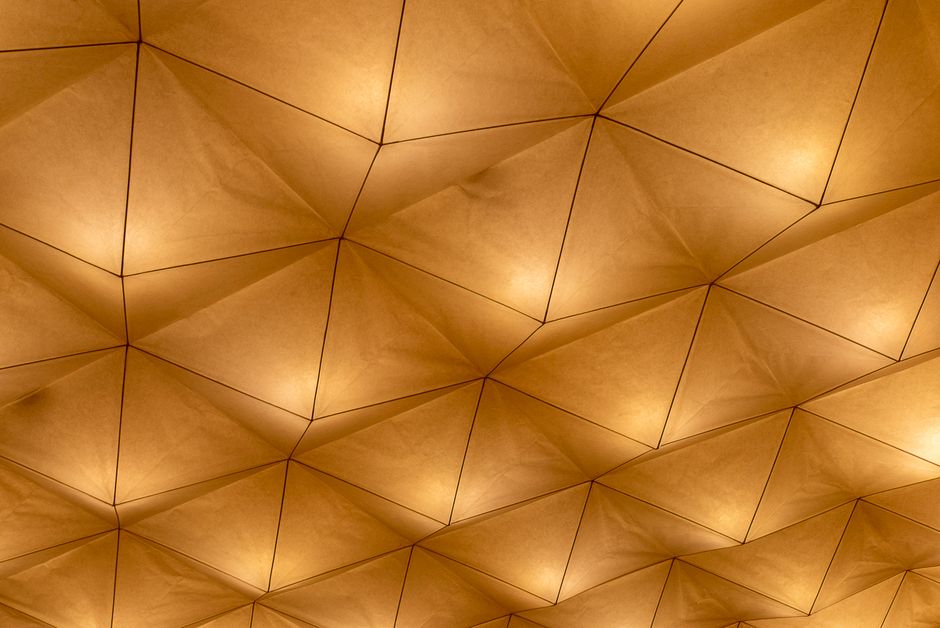 Imagem de um teto com design geométrico em tons de bege e iluminação indireta, ideal para ilustrar ambientes sofisticados e modernos.