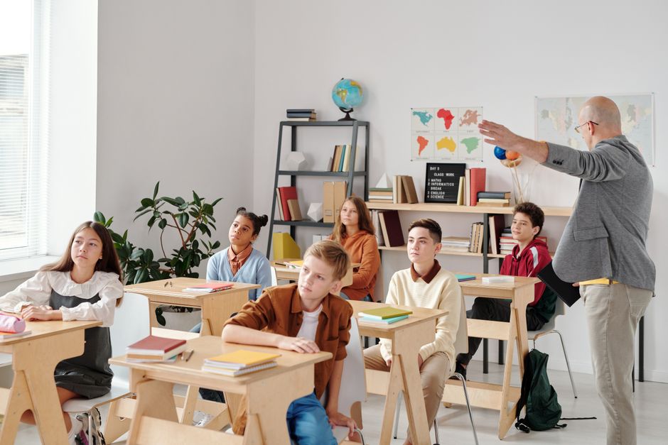 Imagem de uma aula de ciências com um professor demonstrando um modelo de planeta para alunos atentos na sala de aula.
