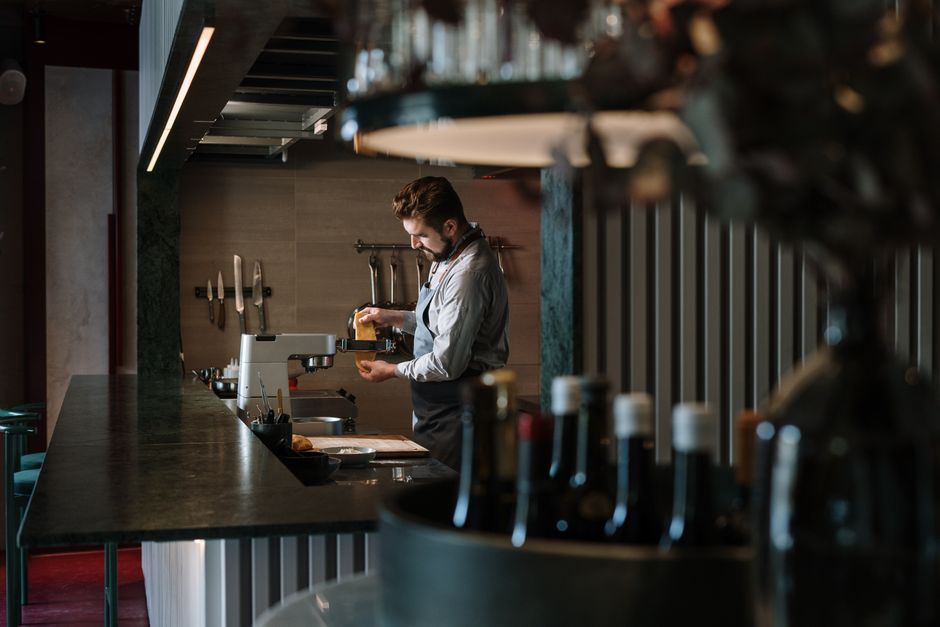 Homem preparando comida em um restaurante com iluminação moderna e ambiente acolhedor.