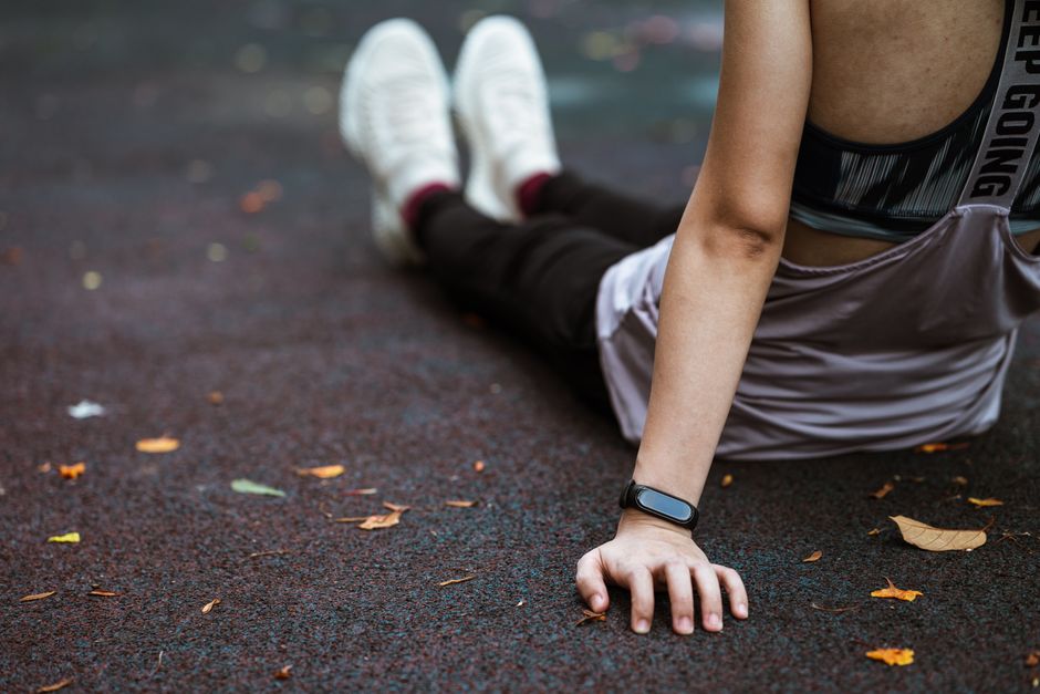 Pessoa descansando após atividade física, sentada no chão com roupas esportivas e com um smartwatch no braço.