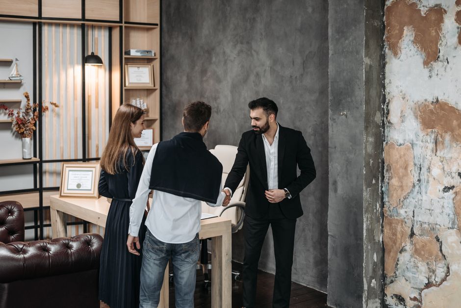 Imagem de uma reunião de negócios onde três pessoas estão trocando um aperto de mãos em um ambiente corporativo moderno.