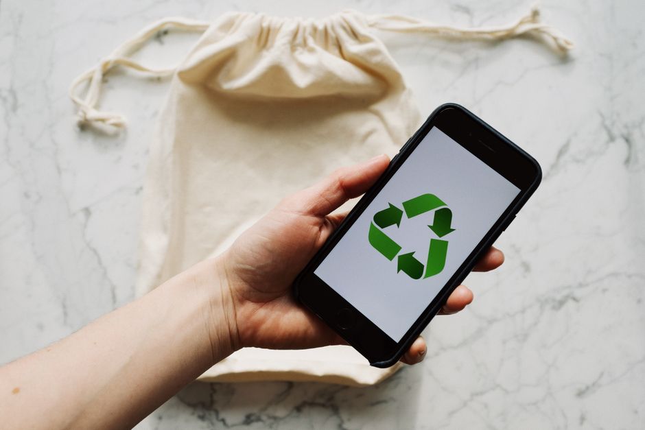 Pessoa segurando um celular exibindo o símbolo de reciclagem, representando sustentabilidade e práticas ambientais responsáveis.