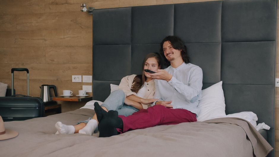 Um casal feliz assistindo TV na cama, criando uma atmosfera de conforto e lazer no quarto.