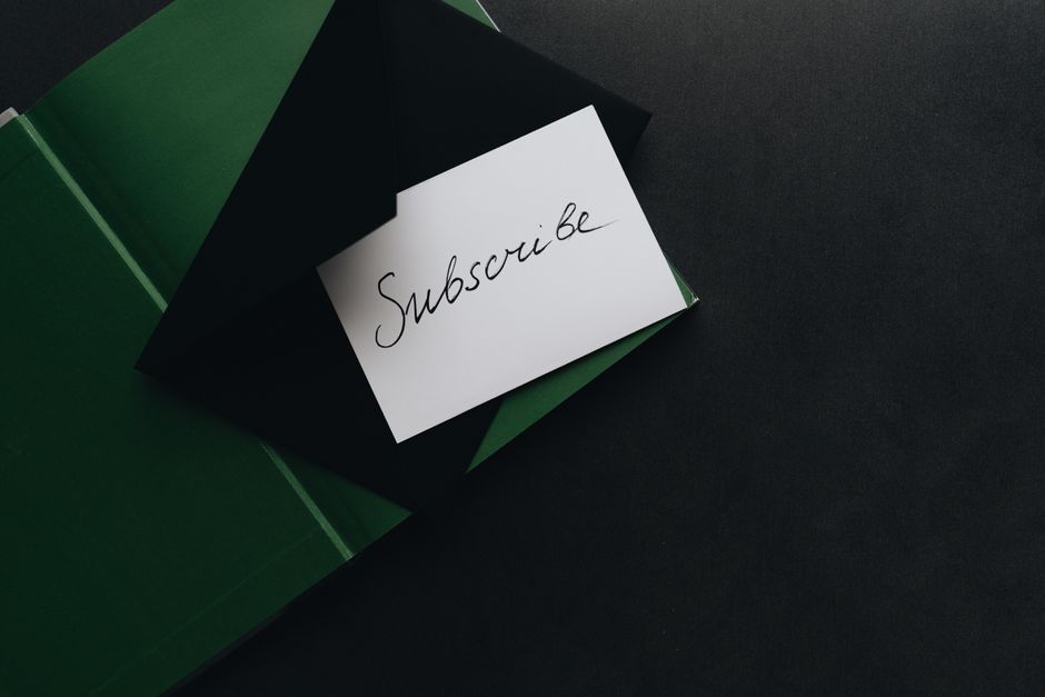 Nota escrita à mão com a palavra 'Subscribe' sobre fundos de papel verde e preto, destacando o tema de engajamento digital.