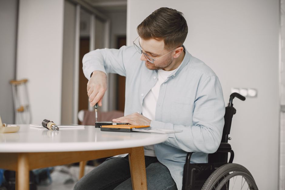 Homem em cadeira de rodas ajustando um móvel ou equipamento em um ambiente de escritório, evidenciando acessibilidade e inclusão no local de trabalho.